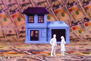 wo symbolic plastic people stand in front of a conventional house against the background of many 100 USD bills