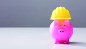 Close-up Of A Pink Piggy Bank With Yellow Hard Hat On White Desk