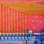 Row of gray gas meters with yellow pipe on red brick wall