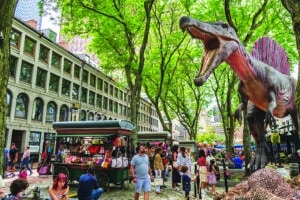 Boston, MA, US-June 11, 2022: People at busy downtown food market and tourist destination with large dinosaur statue in background.