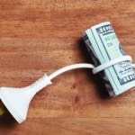 conceptual image of an electrical cord wrapped around a roll of $100 bills