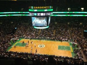 Players for the Celtics and Spurs basketball teams stand underneath the TD Garden's large video projectors, decorated with TD Bank logos, during a 2014 game with a full audience in the stands.