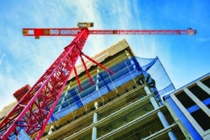 Looking up at the construction site of a high-rise building with red crane in the foreground.