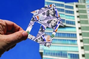 Symbolic house with the image of 100 American dollars in a man's hand against the background of a modern building