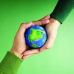 two different people's hands holding a tiny globe against a green background.