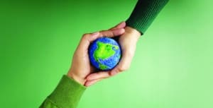 two different people's hands holding a tiny globe against a green background.