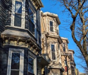 The roofs of several East Boston triple-deckers are seen against a bright blue winter sky.