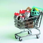 Buy and sell house, property demand and supply on real estate purchasing concept, shopping cart or trolley with full of small cute miniature houses on white background.