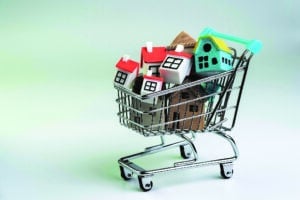 Buy and sell house, property demand and supply on real estate purchasing concept, shopping cart or trolley with full of small cute miniature houses on white background.