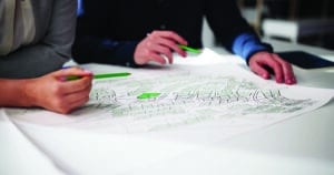 Two people holding pencils while looking at a city plan with some lots highlighted in different colors, like a zoning map.