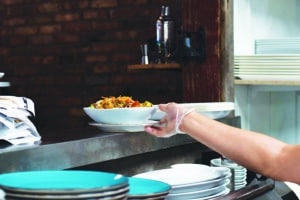 Restaurant kitchen employee placing bowl with fresh salad on window for server to pick up