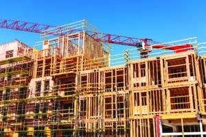 Exterior view of multifamily residential building under construction in Palo Alto, California. A crane is moving materials to a higher level of the building as lower levels are completed.