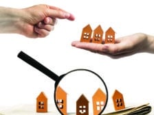 magnifying glass focusing in on a row of houses while one hand floating over them offers a small number of houses to another, which is trying to pick one.