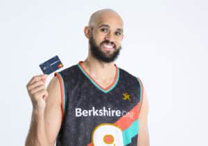 Boston Celtics player Derrick White poses for a photo holding a Berkshire Bank debit card and wearing a promotional Berkshire Bank basketball jersey.