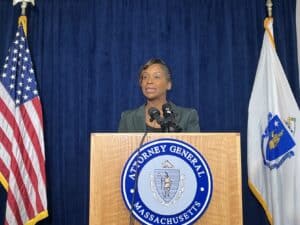 Massachusetts Attorney General Andrea Campbell speaks from behind a podium, flanked by the state and American flags, during a press conference.