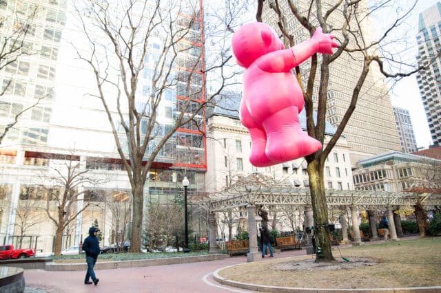 A "Mr. Pink" sculpture installed as though it's climbed a tree in Post Office Square. Its pants-less backside is prominently displayed.