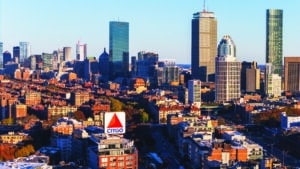 An aerial view of the Boston skyline featuring the iconic CITGO sign. The image captures the city's diverse architecture, including skyscrapers, historic buildings, and the Charles River. The CITGO sign stands out prominently against the backdrop of the cityscape.