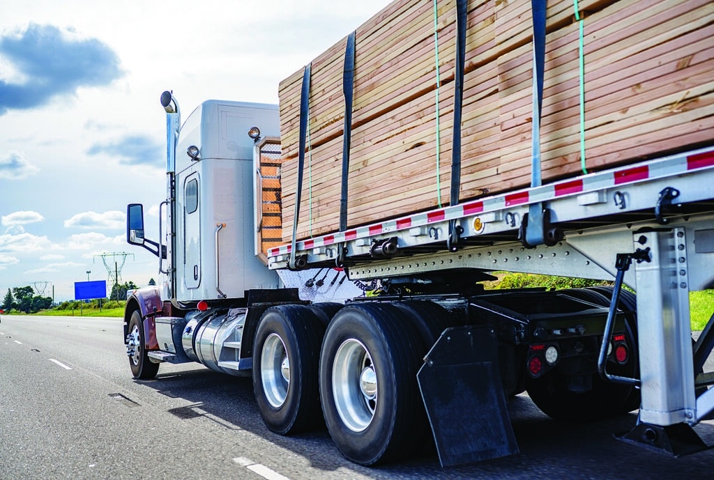 Classic big rig semi truck tractor transporting lumber on the flat bed