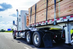 Classic big rig semi truck tractor transporting lumber on the flat bed