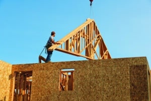 Crane hoisting roof trusses onto the unfinished frame of a residential home.