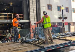 Construction workers get ready to hook a bundle of rebar onto a crane's hook, which will lift the rebar to an upper floor of the 41 Lagrange St. affordable housing tower under construction in spring 2025.