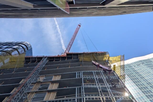 The arm of a crane perched on top of the under-construction 41 Lagrange St. affordable housing tower sticks out into the gap between the building and its neighbor across the street.