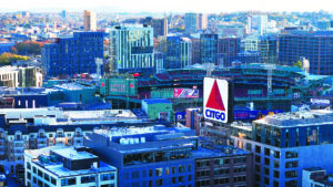 An aerial view of Fenway Park, the historic home of the Boston Red Sox, nestled amidst the cityscape of Boston. The iconic ballpark stands out with its distinctive green facade and the famous "Green Monster" left field wall. The surrounding cityscape provides a vibrant backdrop, highlighting the stadium's integration into the urban fabric of Boston. The image captures the timeless charm of Fenway Park, a beloved landmark and a symbol of baseball history.