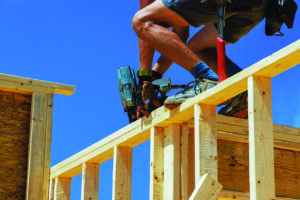 Working with an air nail hammer, framing contractor nails wooden beams